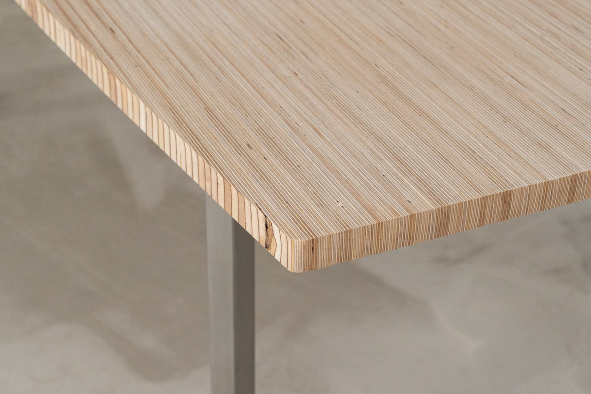 Corner of a Birch Edge Grain Ply oval top on a stainless steel leg, the layers showing along the curved edge